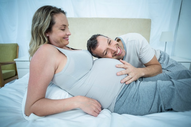 Hombre escuchando el vientre de mujer embarazada en su habitación.