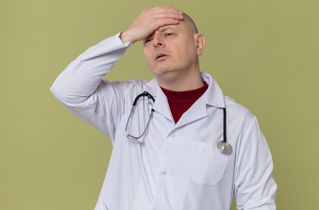 Hombre eslavo adulto decepcionado en uniforme médico con estetoscopio poniendo la mano en la frente y mirando a un lado