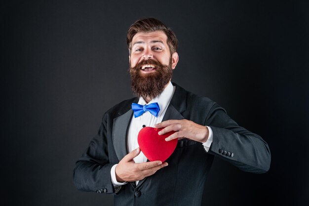 Hombre de esmoquin feliz con barba mantenga amor romántico corazón feliz día de san valentín