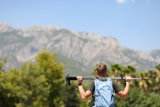 El hombre se para con la espalda y sostiene palos escandinavos en la cima del concepto de marcha nórdica de montaña