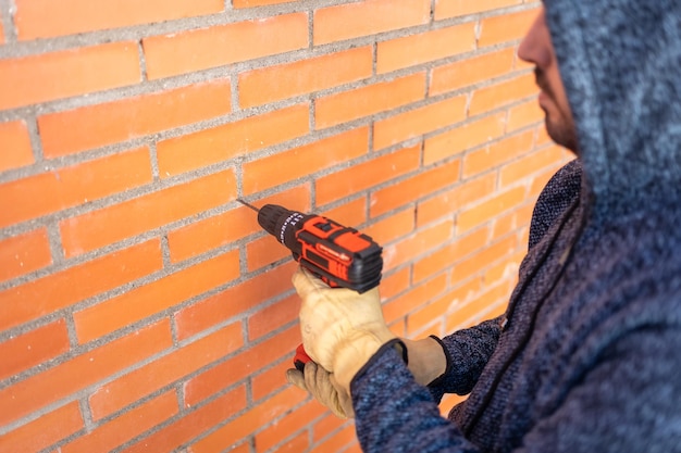 Hombre de espaldas haciendo agujeros con un taladro eléctrico en la pared de ladrillo