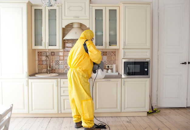 Un hombre especialista en control de insectos con un traje protector amarillo rocía las paredes del apartamento