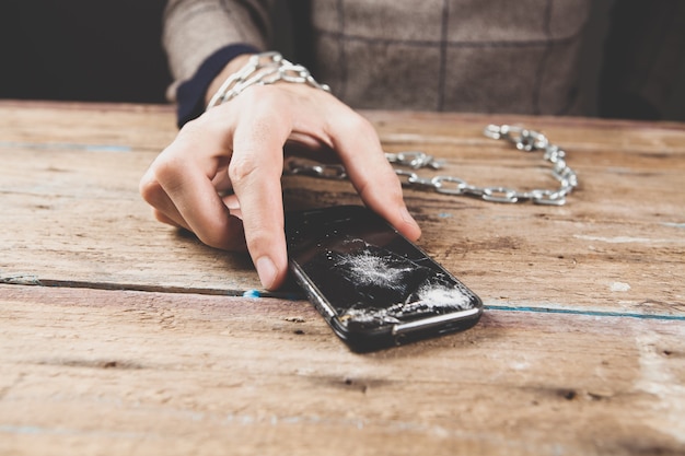 Un hombre esposado sosteniendo un teléfono roto.