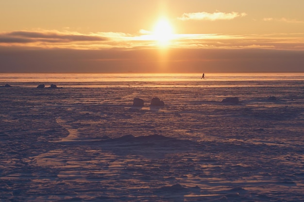 Foto un hombre con esquís cruza un cuerpo de agua congelado al atardecer