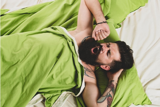 El hombre está acostado en la cama y disfruta de la mañana. El hombre tiene problemas para dormir. El hombre barbudo se despierta en b ...