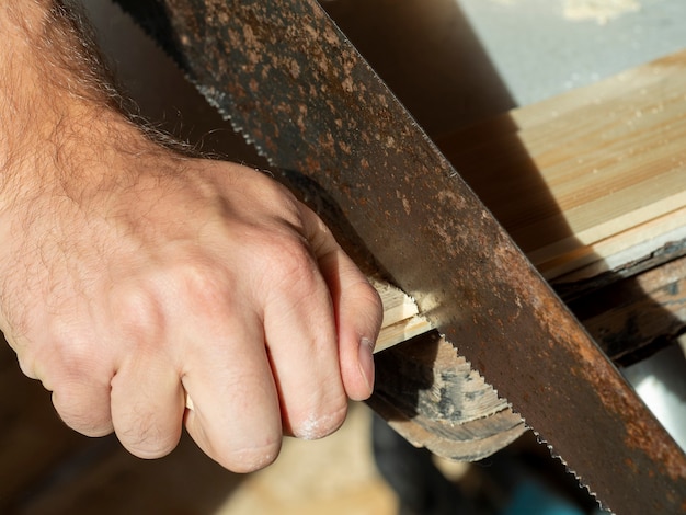 Un hombre está aserrando una tabla con una sierra de mano. Concepto de carpintería.