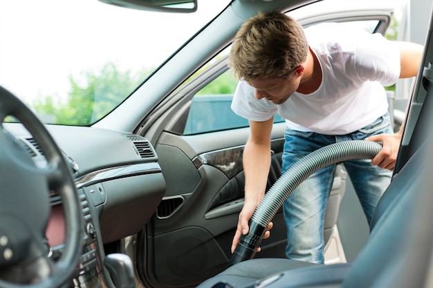 El hombre está aspirando o limpiando el auto