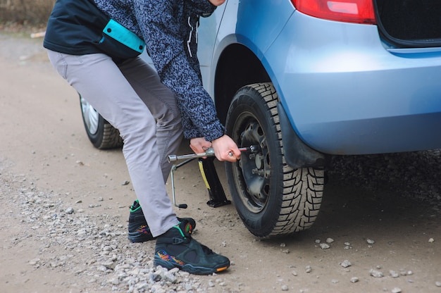 El hombre está cambiando el neumático con la rueda en el auto