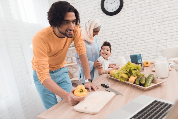 El hombre está cocinando detrás de él, de pie a su esposa en hijab e hijo.