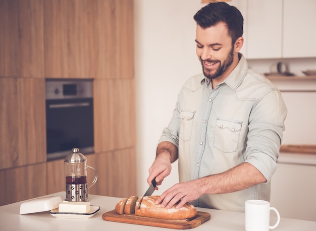 El hombre está cortando pan y sonriendo mientras hace sándwiches