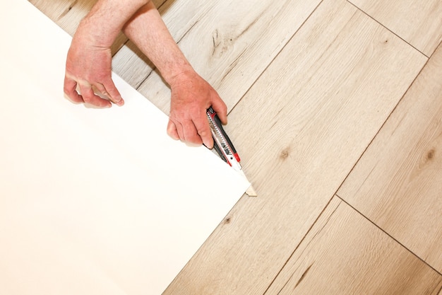 El hombre está cortando papel tapiz en rollo en el piso. Mantenimiento de obras de reparación de reforma en el piso. Restauración en interior.