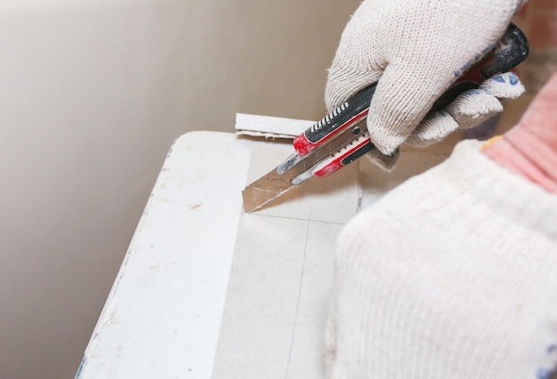 El hombre está cortando una placa de yeso con un cuchillo utilitario Reparación de mantenimiento trabajos de renovación en el piso Restauración interior Panel de paneles de yeso