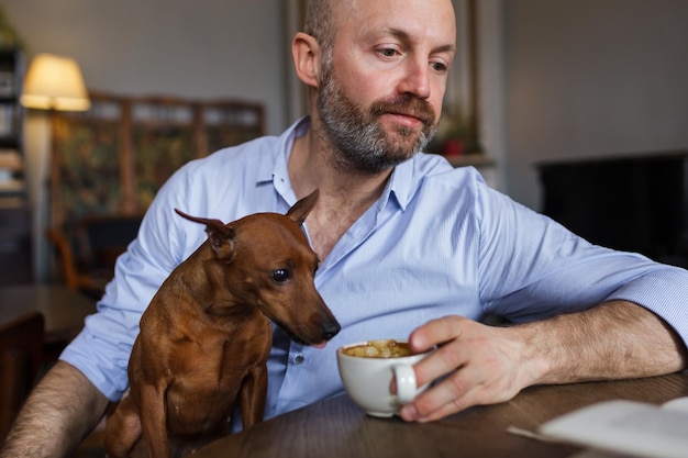 El hombre está descansando con su perro Lee el libro y el perro prueba discretamente el café de su taza