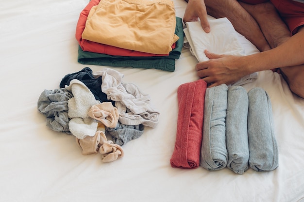 El hombre está doblando y arreglando la ropa en la cama.