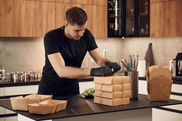 El hombre está empaquetando comida en las cajas ecológicas de papel en el restaurante interior