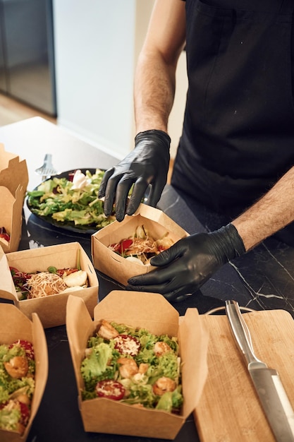 El hombre está empaquetando comida en las cajas ecológicas de papel en el restaurante interior