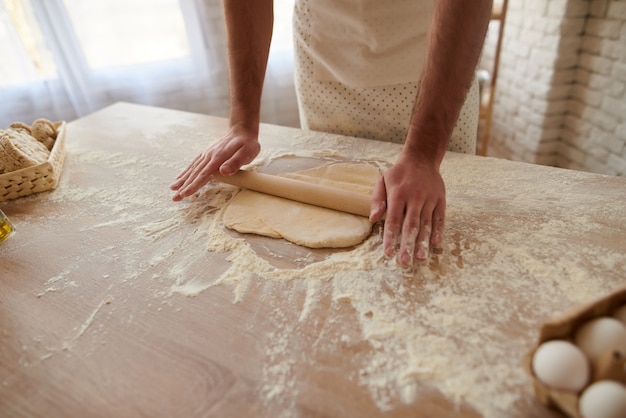 El hombre está extendiendo la masa sobre la mesa de la cocina.