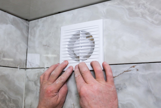 El hombre está haciendo el proceso de restauración de la ventilación del ventilador del baño de la pared