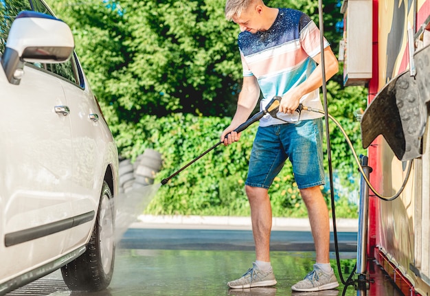 El hombre está lavando el coche con agua a alta presión