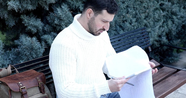 Un hombre está leyendo un periódico sentado en un banco.