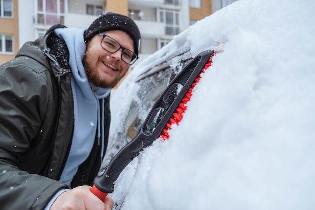 Un hombre está limpiando un automóvil cubierto de nieve.