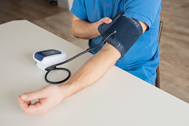 El hombre está midiendo la presión arterial con el monitor en casa.