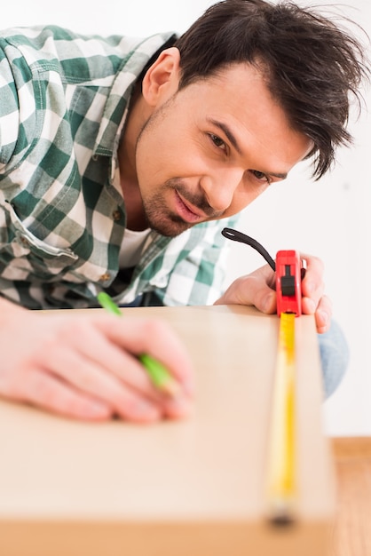 El hombre está midiendo el tablero de madera con cinta métrica.