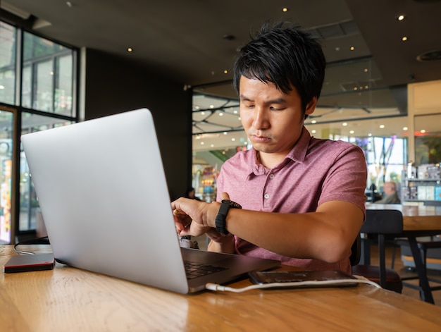 El hombre está mirando su reloj inteligente con computadora portátil en la cafetería