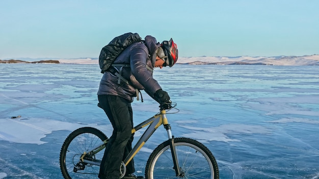 El hombre está montando en bicicleta en el hielo Hielo del lago Baikal congelado El jinete está vestido con una chaqueta negra, un casco de mochila de ciclismo Neumáticos cubiertos con picos especiales El niño viajero está montando en bicicleta