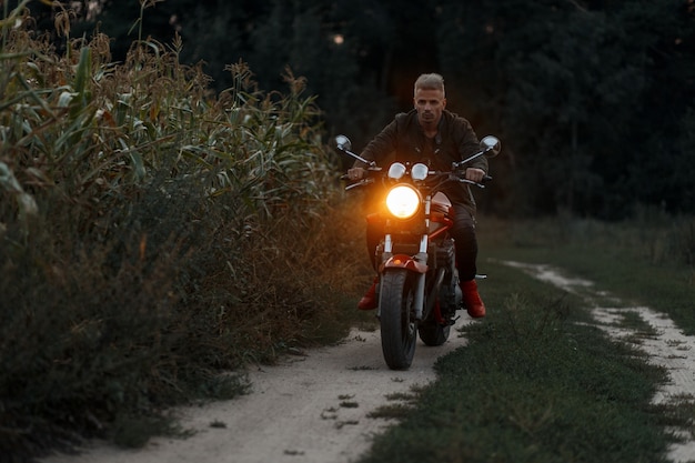 El hombre está montando una motocicleta con luz en un campo de maíz en la noche