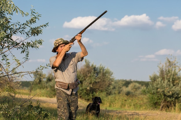 Un hombre está parado con armas y perros de caza rastreando el juego.