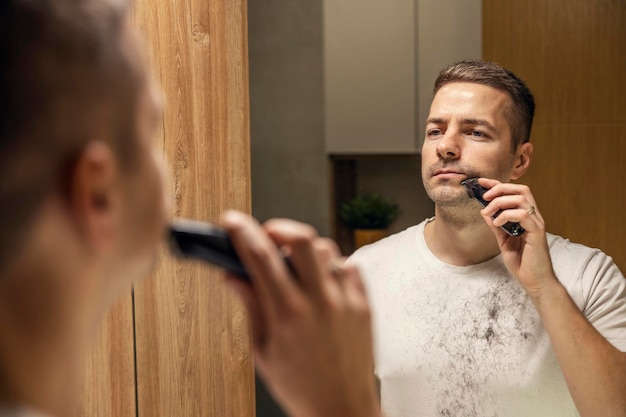 Un hombre está parado en el baño y afeitándose la barba en casa.