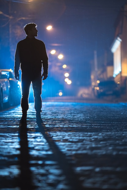 El hombre está parado en el camino de la lluvia. Tarde por la noche. Disparo con teleobjetivo