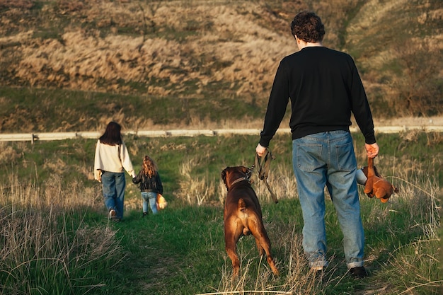 el hombre está parado en la carretera con un perro grande y el juguete de un niño, su esposa y su hijo lo están dejando