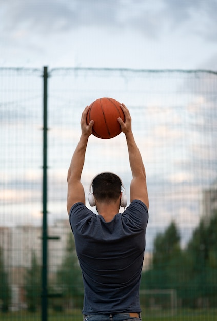 Un hombre está parado con la espalda contra el fondo de un campo de deportes y sostiene una pelota de baloncesto en sus manos