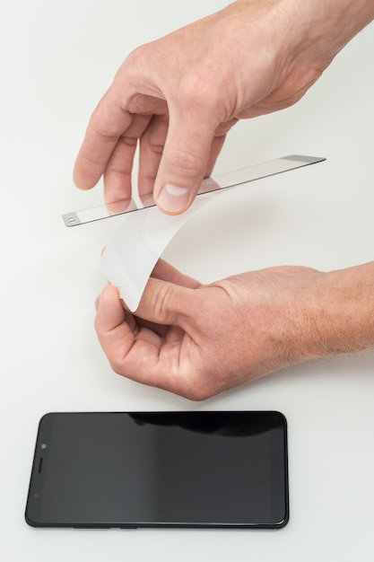 Un hombre está pegando un vidrio protector en la pantalla de un teléfono inteligente.