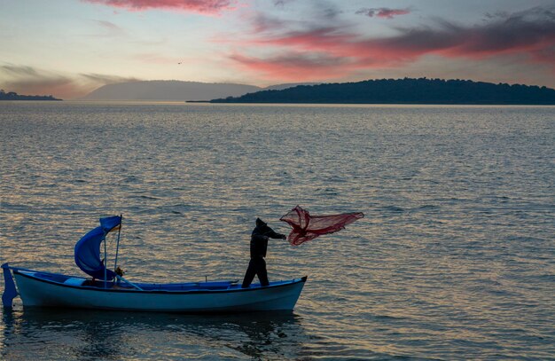 un hombre está pescando en un barco con una bandera roja en él
