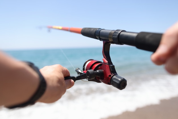 El hombre está pescando con línea en primer plano de la orilla del mar