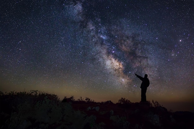 Un hombre está de pie junto a la galaxia de la Vía Láctea apuntando a una estrella brillante