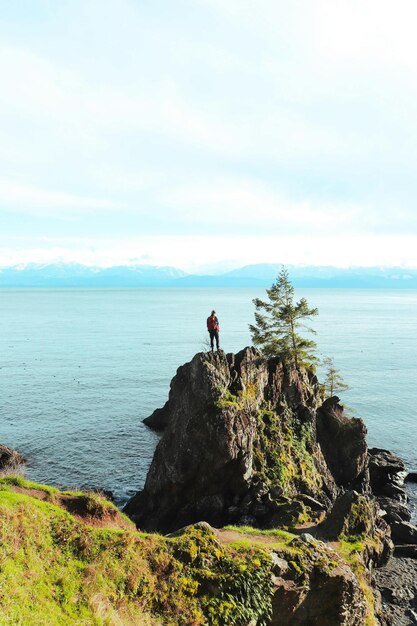 un hombre está de pie en una roca con vistas al océano y el océano