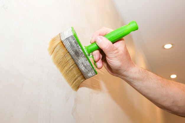 El hombre está poniendo pegamento en la pared con un cepillo. Papel tapiz para colgar. Mantenimiento de obras de reparación de reforma en el piso. Restauración en interior.