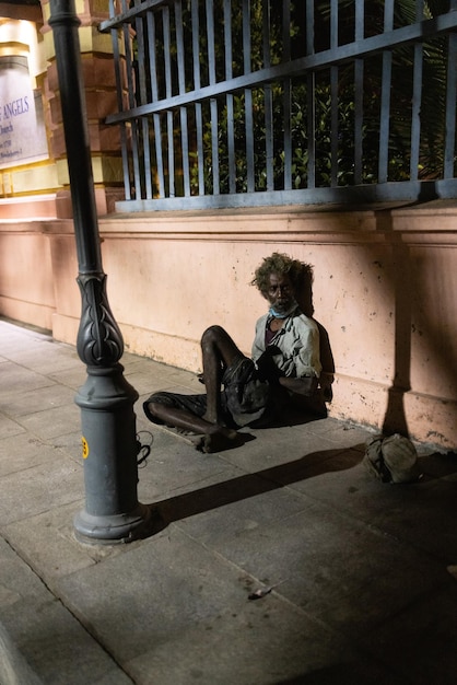 Un hombre está sentado en la calle frente a un poste de luz.