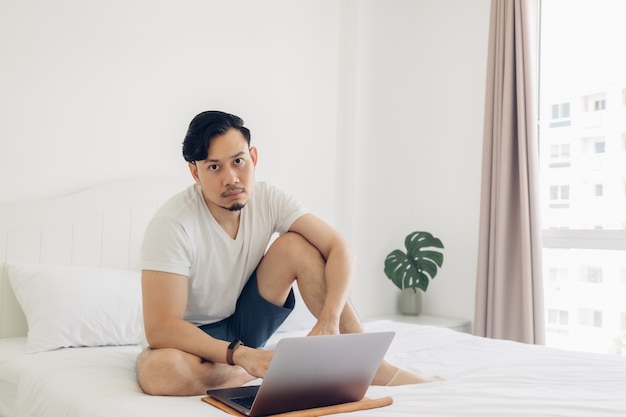 El hombre está sentado en la cama y trabaja en su computadora portátil.