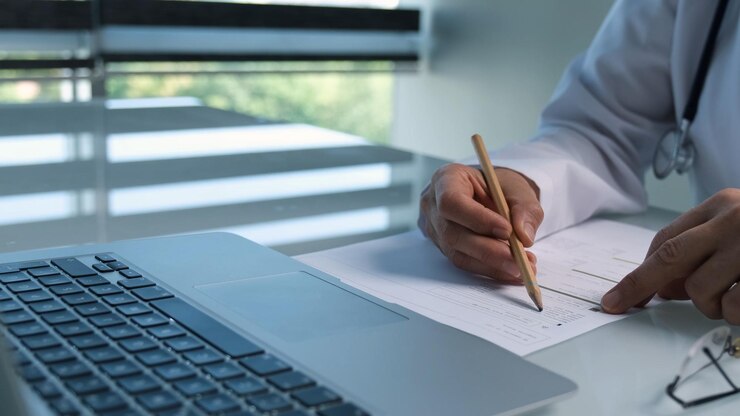 Un hombre está sentado en un escritorio con una computadora portátil y un bolígrafo en la mano.