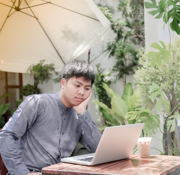 Un hombre está sentado en una mesa con una computadora portátil y una taza de café.