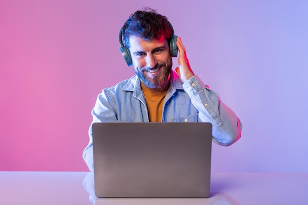 Un hombre está sentado en una mesa enfocado en la pantalla de su portátil con auriculares que parece estar trabajando