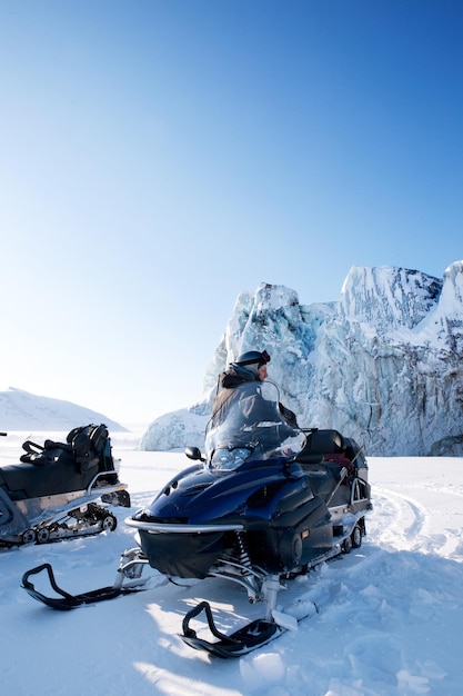 un hombre está sentado en una moto de nieve con una montaña detrás de él