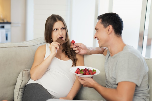 El hombre está sentado a su lado. Comen fresas y dulces.