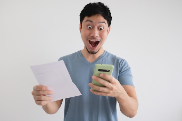 El hombre está sorprendido por la factura y el teléfono inteligente en la pared aislada.