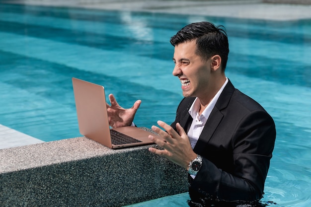 El hombre está súper enojado con la computadora portátil mientras está de pie en la piscina